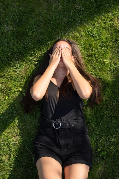 Молодая кавказская девушка сидит на траве и закрывает лицо — стоковое фото