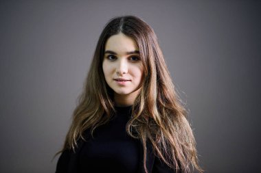 Gri arka planda poz veren kahverengi saçlı genç beyaz kız