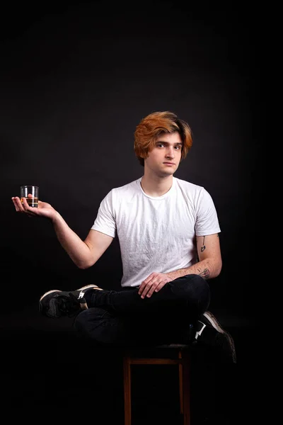 Молодой кавказский взрослый человек с светлыми волосами, держащий виски в руке — стоковое фото