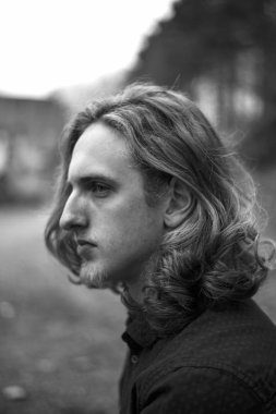 Uzun saçlı beyaz beyaz genç bir adamın siyah beyaz portresi