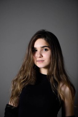 Gri arka planda poz veren kahverengi saçlı genç beyaz kız