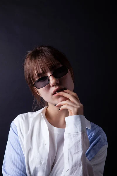 Белая девушка в белой рубашке в черных солнцезащитных очках позирует в студии — стоковое фото