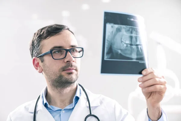 Dentista masculino caucásico analizando la radiografía en el gabinete dental — Foto de Stock