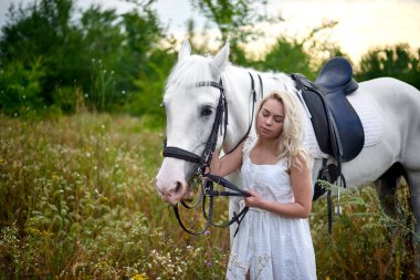 Beyaz elbiseli kız sahada bir at tutan