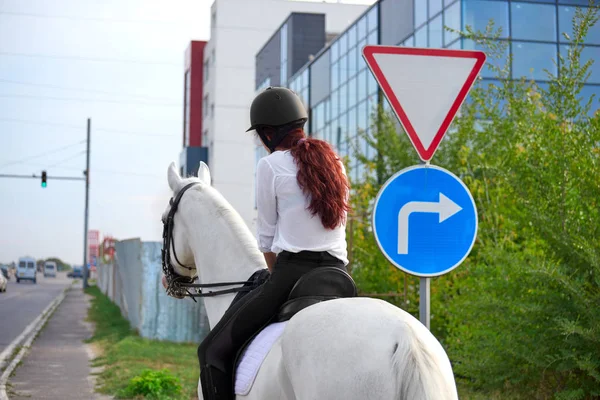 Fille en tenue équestre chevauchant un cheval dans la ville près de la traite — Photo