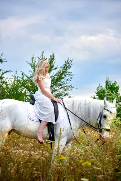 Flicka i vit klänning ridning en häst i fältet — Stockfoto