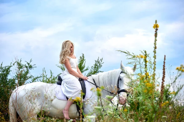 Flicka i vit klänning ridning en häst i fältet — Stockfoto