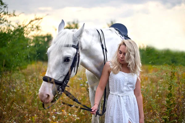 Fille en robe blanche tenant un cheval dans le champ — Photo