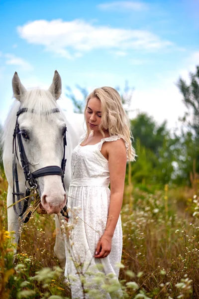 Flicka i vit klänning som håller en häst i fält — Stockfoto