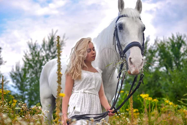 Fille en robe blanche tenant un cheval dans le champ — Photo