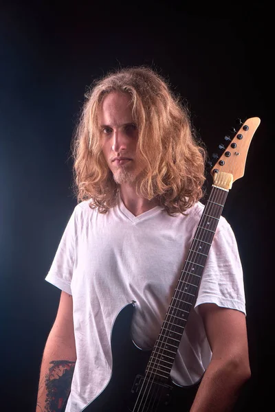 Caucasian man with blonde hair holding his black guitar