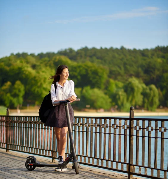 Teenager-Gymnasiastin fährt ihren Elektroroller in der Nähe des Sees — Stockfoto