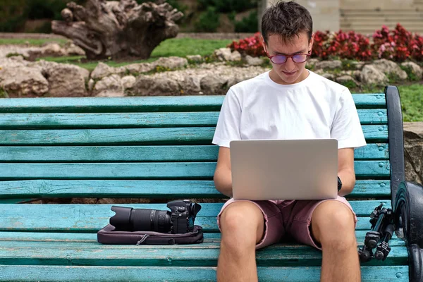 Genç fotoğrafçı parkta bir dizüstü bilgisayar üzerinde çalışıyor