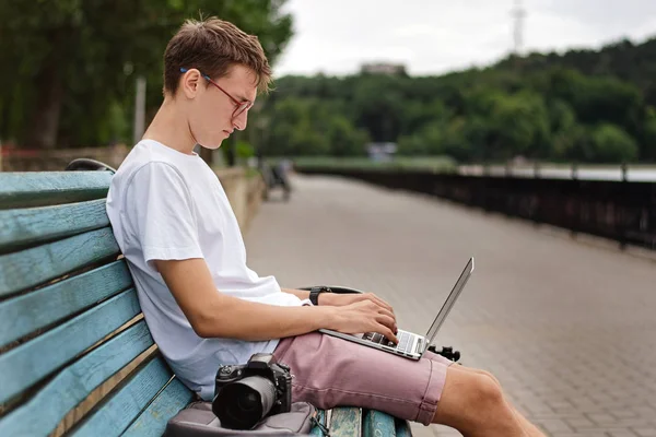 Genç fotoğrafçı parkta bir dizüstü bilgisayar üzerinde çalışıyor