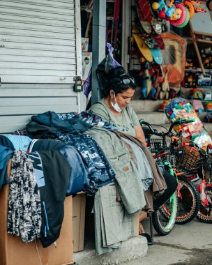 CHISINAU, MOLDOVA - 18 Haziran 2020: Yerel bir pazarda kıyafet ve bisiklet satan yaşlı kadın. Koruyucu tıbbi maske takmıyor.