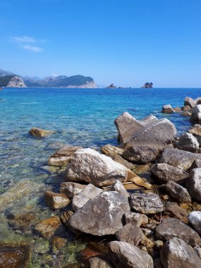 Adriyatik denizi ve tepelerinin kayalık kıyıları, Karadağ 'ın Petrovac kentindeki arka planda yeşillikle kaplı