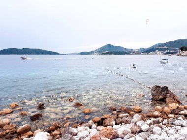Adriyatik 'in kayalık kıyıları, arka planda görünen şehir ve tepeler, Karadağ' da suda yüzen bir tekne