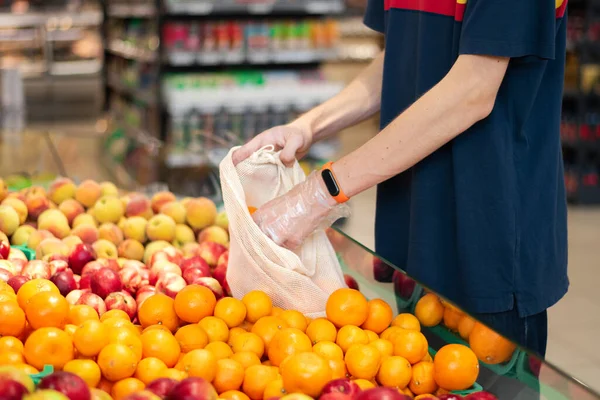 A man in supermarket with eco bag taking tangerines