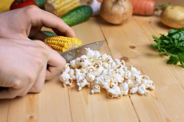 Tahta masada mısır koçanı dilimleyen bir adam, sebzeler, abur cubur fikirleri.