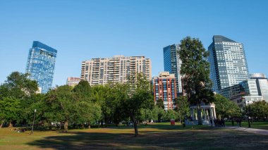 BOSTON, MASSACHUSETTS - 5 Ekim 2019: az sayıda yürüyen insanın olduğu bir park, bir sürü ağaç, çardak, arka planda yüksek binalar