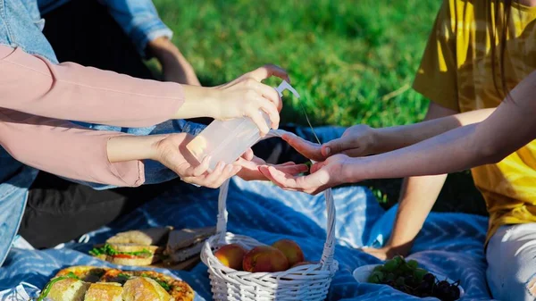 Group of friends disinfecting hands at a picnic blanket with goodies, in a park during the pandemic in Chisinau, Moldova