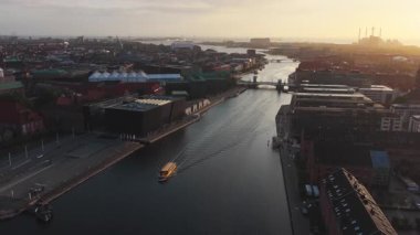 Danimarka 'nın Kopenhag limanındaki tekneler ve modern binalarla altın saat boyunca Nyhavn Kanalı ve şehir manzarasının insansız hava aracı görüntüsü.