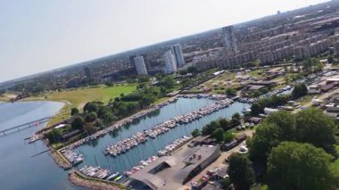 Danimarka, Kopenhag 'daki yeşil sahil ve konut blokları ile çevrili yelkenli tekneleriyle dolu marinanın insansız hava aracı görüntüsü.
