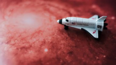 Kırmızı bir galaksinin arka planına yerleştirilmiş minyatür bir oyuncak uzay mekiğine yakın çekim