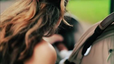 Yeşilliklerle çevrili bir bankta otururken bebek arabasını tutan kıvırcık saçlı bir kadın.