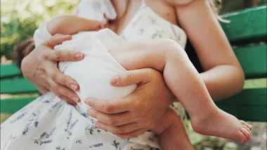 Bir annenin bebeğini yeşil bir bankta gündüz vakti emzirdiği o hassas an.