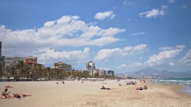 Alicante, İspanya - 20 Mayıs 2025: Dağılmış güneş banyosu, palmiye ağaçları ve Alicante ufuk çizgisi ile Costa Blanca 'da geniş bir sahil manzarası