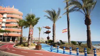 Benidorm, İspanya - 25 Mayıs 2025: Arkaplanda İspanyol bayrağı ile deniz kenarında dengelenen pas tonlu ton balığı heykellerinin uzak görünümü