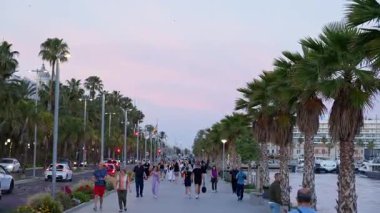 Alicante, İspanya - 26 Mayıs 2025: Gezginler gün batımında sallanan yatlarla palmiye püsküllü iskeleyi paylaşıyorlar