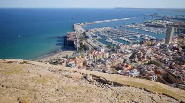 Sweeping view from the castle across Playa del Postiguet, the marina packed with yachts, and the long breakwaters of the Port of Alicante