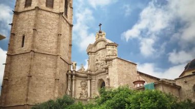 Low angle view of the Baroque main portal and adjacent bell tower of Valencia Cathedral, framed against a bright blue sky in Valencia, Spain