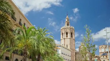 Daytime view of El Micalet bell tower rising above palm trees and surrounding historic roof in the Cathedral precinct, Valencia, Spain