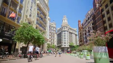 Valencia, Spain - May 29, 2025: Cyclists and pedestrians on a pedestrian boulevard leading toward the landmark towered buildings of Plaza del Ayuntamiento