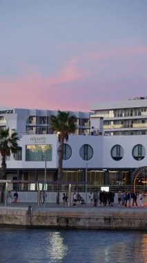 Alicante, Spain - May 30, 2025: A line of luxury boats rests with the Melia Alicante as a backdrop in soft pink skies. Vertical