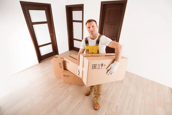 Mover man holding big box of items in empty apartment. Delivery service backdrop.