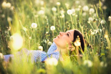 Yaz sahne. Kız beyaz dandelions akşam zaman zevk. Genç kadın açık havada çayır üzerinde rahatlatıcı.