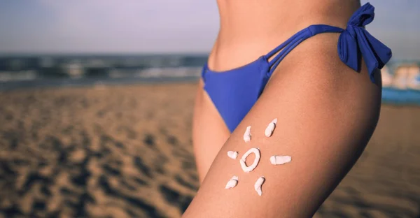 Sun cream on girl tanned skin close-up. Woman leg with cream on beach background with copy space. Skin care on beach background.