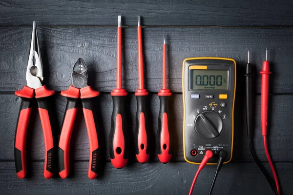 Professional tools for electrician. Screwdrivers, nippers, tester on black wooden background. Studio shot. View from above. Industrial backdrop.