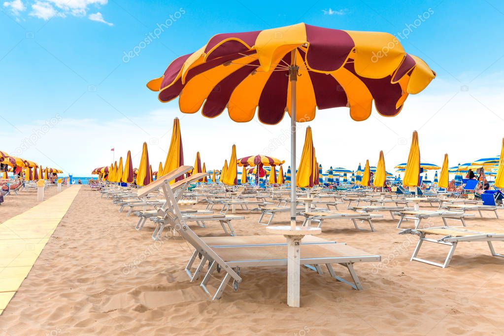 Yellow sun umbrella on beach on blue sky background. Rimini beach, Italy. Summer vacation.