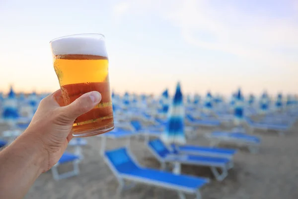 Beer on beach. Hand holding plastic glass of beer on beach background. Evening relaxation in Rimini, Italy.