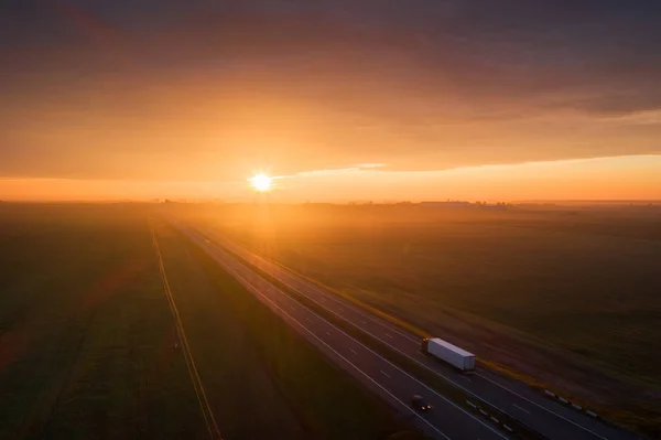 Truck on highway in the morning. Cargo transportation background. Aerial transportation landscape. Colorful sky with rising sun over freeway.