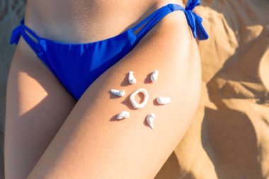 Güneş koruyucu güneş kremi. Üstten görünüm kız bikini ve güneş güneş koruma kum zemin üzerine krem ile bacak üzerinde çizilmiş. Cilt bakım kavramı. Cilt Bakımı arka plan. Emniyet tan.