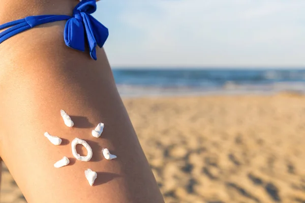 Sunscreen suntan cream. Sun drawing. Sunblock cream on tanned skin closeup. Concept for uv rays protection. Tanned female leg with sun drawing with sunscreen lotion on beach and sea background.