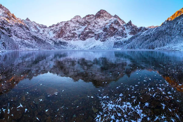Winter landscape. Mountains reflected in frozen lake. Mountain lake covered with clear transparent ice. Winter natural background.