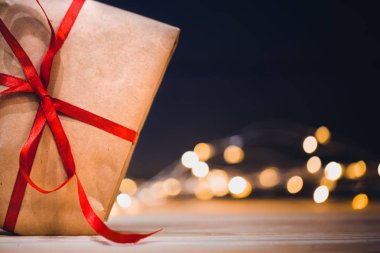 Zanaat kutusu bokeh ışıkları ile koyu arka plan üzerinde kırmızı kurdele Fiyonklu hediye. Metin tebrik için alanı kopyalayın. Tatil arka plan.