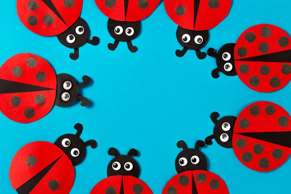 Background for the advertisement of kids educational activities with copy space in the middle. Handmade paper ladybugs. Toy ladybugs on a blue background.